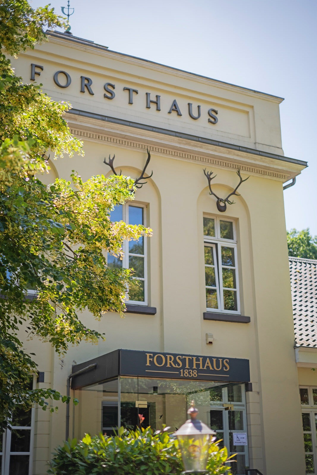 Hausfassade mit Schriftzug Forsthaus, zwei Geweihen über den Fenstern und Glasvordach am Eingang